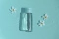 Cosmetic bottle on blue background with water and flowers. Royalty Free Stock Photo