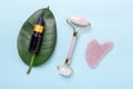 Cosmetic bottles, face serum, facial massage roller and Gua Sha massager on blue background. Anti age, lifting and toning