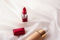 Beige tonal cream bottle make-up fluid foundation base and red lipstick on silk background, cosmetics products as luxury beauty