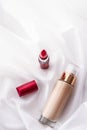 Beige tonal cream bottle make-up fluid foundation base and red lipstick on silk background, cosmetics products as luxury beauty