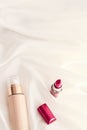 Beige tonal cream bottle make-up fluid foundation base and red lipstick on silk background, cosmetics products as luxury beauty