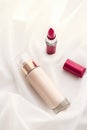 Beige tonal cream bottle make-up fluid foundation base and red lipstick on silk background, cosmetics products as luxury beauty