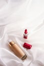 Beige tonal cream bottle make-up fluid foundation base and red lipstick on silk background, cosmetics products as luxury beauty