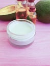 Cosmetic cream, avocado health oil therapy on pink wooden background