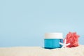 Cosmetic cream in blue glass bottle with Starfish and pink seaweed on the sand on blue background, copy space. UVA and UVB Royalty Free Stock Photo