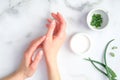 Cosmetic cream on female hands, jar with aloe vera cream and green sliced stems on marble background. Woman applying organic Royalty Free Stock Photo