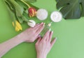 Cosmetic cream hand tulip flower lifestyle creative manicure essence monstera leaf on green colored paper Royalty Free Stock Photo