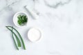 Cosmetic cream jar and green sliced stems aloe vera on marble background. Organic moisturizer face cream. Facial skin care and