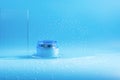 Cosmetic cream in a jar, splashes and drops of water on a blue background. Face, body, hair care Royalty Free Stock Photo