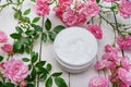 Cosmetic cream surrounded by pink roses on white wooden background, body skin care Royalty Free Stock Photo