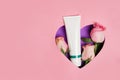 Cosmetic cream white tube with flowers roses in violet heart . pink background with copy space Royalty Free Stock Photo