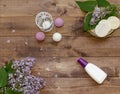 Cosmetic flat lay with a bouquet flowers lilac.Spa set of bottle cream, handmade bombs, candle with birdcage, sponges on wood Royalty Free Stock Photo