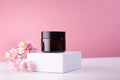 Cosmetic jar for cream of amber glass on white podium and pink wall with fresh spring flowers. Template for branding identity.