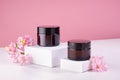 Cosmetic jars for cream of amber glass on white podium and pink wall with fresh spring flowers. Template for branding identity.