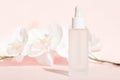 Cosmetic liquid mockup in transparent bottle on pastel pink background with flowers. cosmetics branding