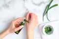 Cosmetic lotion bottle on female hands and green sliced stems aloe vera on white marble table. Woman applying organic moisturizing Royalty Free Stock Photo