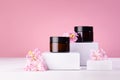 Cosmetic mockup - jars for cream of amber glass on white podiums with pink spring flowers. Template for branding identity.