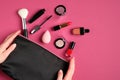 Cosmetic pouch with professional decorative cosmetics and makeup tools in female hands over pink background. Top view, flat lay. Royalty Free Stock Photo