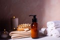 Cosmetic product in gllass bottle, towels, wisp, massager and burning candles on textured background. Royalty Free Stock Photo