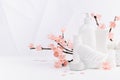 Cosmetic products in white bottles, branch of spring pink sakura flowers, toiletry for makeup facial skin care in white interior