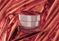 Cosmetic rose gold jar with cream on beautifully folded foil background.