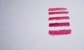 swatches of five red shades of lipstick on white paper on the right side