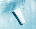 Cosmetic sunscreen product on blue water surface with splashes and drops. Body care health concept. Flat lay top view Royalty Free Stock Photo