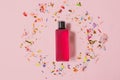 Cosmetics packaging design concept or mock-up with blank transparent bottle with pink perfume on a pink surface surrounded by fes