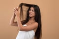 Cosmetics for problems, dry and brittle hair. Upset young armenian woman cannot comb long hair, beige background