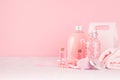 Cosmetics products for bath, spa - essential oil, bath salt, cream, liquid soap, towel in delicate pastel pink bathroom interior.
