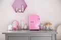 Cosmetics refrigerator and skin care products on grey chest of drawers indoors