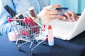 Cosmetics and woman`s essentials in shopping cart with woman usi