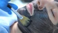 Cosmetologist applying carbon nanogel to skin of woman`s face using brush.