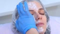 Cosmetologist is applying cream with anaesthesia on patient's face, closeup hand.