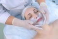 Cosmetologist applying facial moisturizing mask on woman face in beauty clinic.