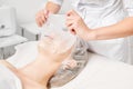 Cosmetologist applying sheet mask on woman face for rehydrate face skin, procedure in beauty salon