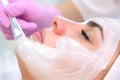 Cosmetologist is applying white mask on woman client face in beauty clinic.