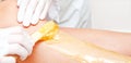Cosmetologist beautician waxing female legs in the spa center beauty salon closeup