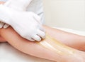 Cosmetologist beautician waxing female legs in the spa center beauty salon depilation epilation
