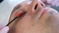 Cosmetologist is bruching eyelashes of man usinf mascara brush, closeup view.