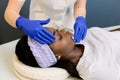 Cosmetologist cleaning face of a young African woman with a cotton pads. Removing cosmetics with hygienic discs.