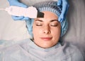 Cosmetologist cleaning woman forehead with ultrasonic scrubber.