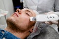 Cosmetologist is cleaning the young man& x27;s face from acne and scars by ultrasonics