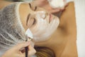 Cosmetologist covering young womans face with moisturizing mask with brush