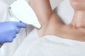 The cosmetologist does the laser hair removal procedure in the armpit zone, to a young woman in a beauty salon