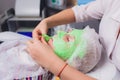 cosmetologist with the help of a special make-up brush makes a therapeutic spa mask from green algae against aging of a Royalty Free Stock Photo