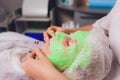 cosmetologist with the help of a special make-up brush makes a therapeutic spa mask from green algae against aging of a Royalty Free Stock Photo