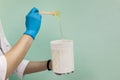 The cosmetologist holds a jar of sugar wax, shows texture of paste with a spatula