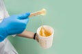 The cosmetologist holds a jar of sugar wax, shows texture of paste with a spatula