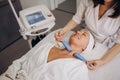 A cosmetologist makes a microcurrent facial therapy to a woman in a beauty salon.